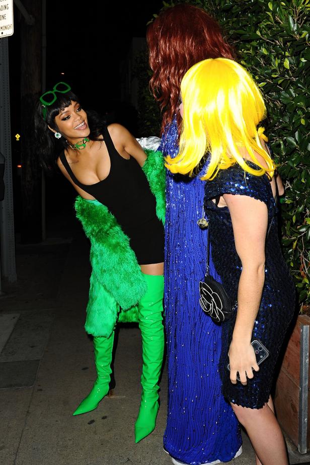 Rihanna in einem schwarzen Kleid, grünen Stiefeln und einer grünen Pelzjacke mit Freunden.