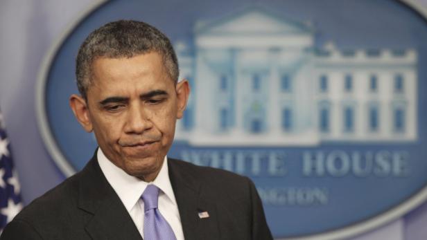 Barack Obama steht vor einem Hintergrund des Weißen Hauses und blickt nach unten.