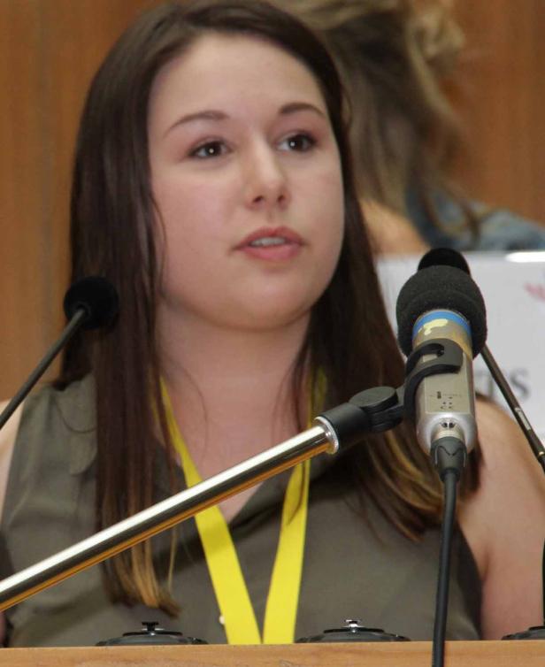 Eine junge Frau spricht bei einer Konferenz vor mehreren Mikrofonen.