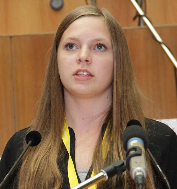 Eine junge Frau mit langen blonden Haaren spricht an einem Mikrofon.