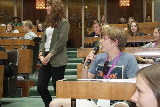 Ein junger Mann spricht in einem Auditorium in ein Mikrofon.