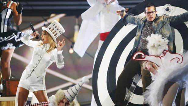 Taylor Swift tritt in einem weißen Anzug und Zylinder auf einer Bühne auf.