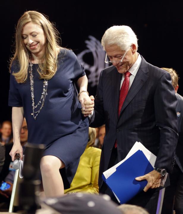 Bill Clinton hält die Hand seiner Tochter Chelsea auf einer Bühne.