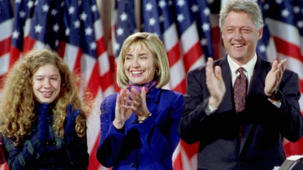 Bill Clinton, Hillary Clinton und ihre Tochter Chelsea applaudieren vor US-Flaggen.