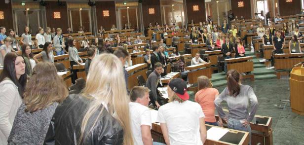 Eine Gruppe junger Leute sitzt in einem großen Saal mit Holzbänken.