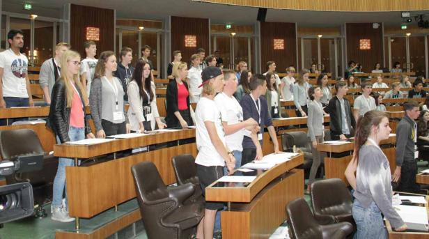 Eine Gruppe junger Leute steht in einem großen Saal mit Holztäfelung.