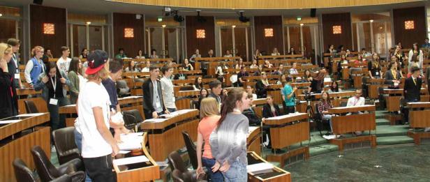 Jugendliche sitzen und stehen im Plenarsaal des Parlaments.