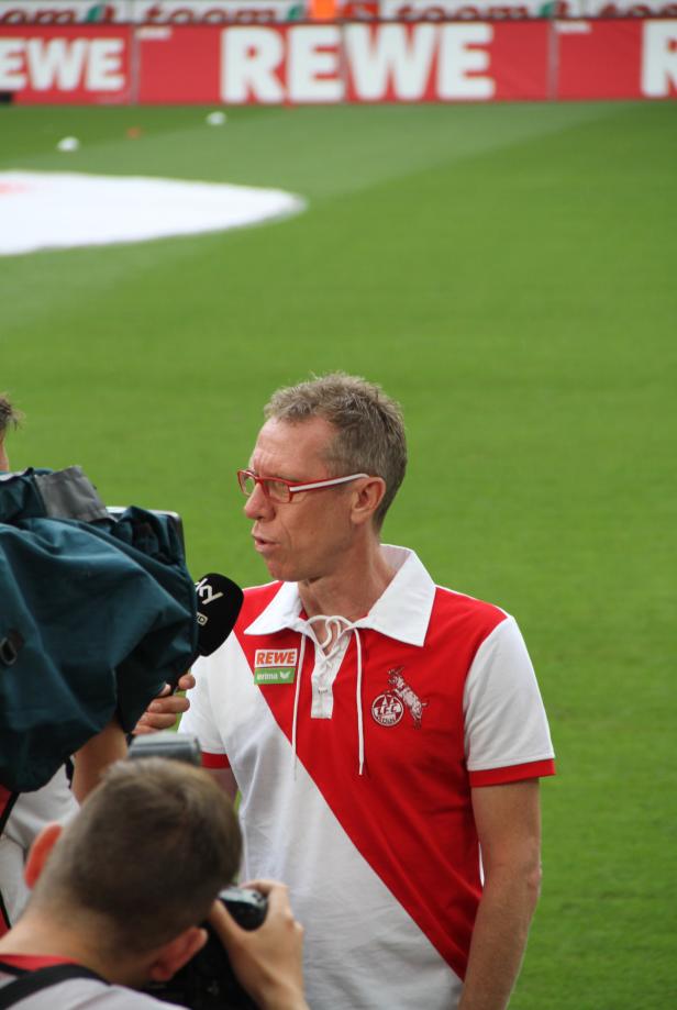 Ein Mann mit roter Brille wird vor einem Fußballstadion interviewt.