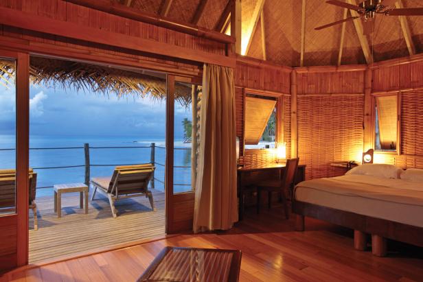 Blick aus einem strohgedeckten Bungalow auf eine Terrasse mit Meerblick.