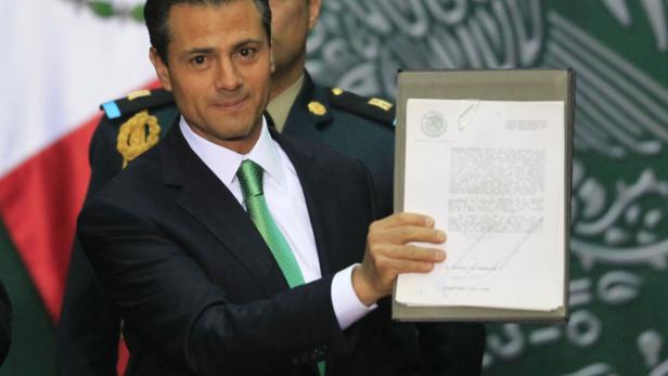 Enrique Peña Nieto präsentiert ein unterzeichnetes Dokument vor einem mexikanischen Hintergrund.
