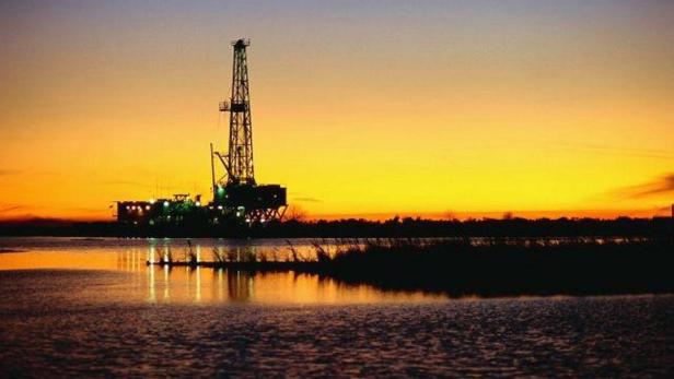 Ein Ölbohrturm steht im Wasser bei Sonnenuntergang.