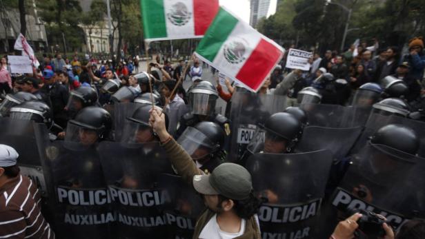 Polizisten in Schutzausrüstung stehen vor einer Menschenmenge mit mexikanischen Flaggen.