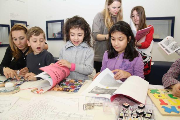 Eine Gruppe Kinder und Erwachsene sitzen an einem Tisch und beschäftigen sich mit Büchern und Spielen.