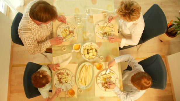 Eine Familie isst gemeinsam Spargel und Kartoffeln am Tisch.