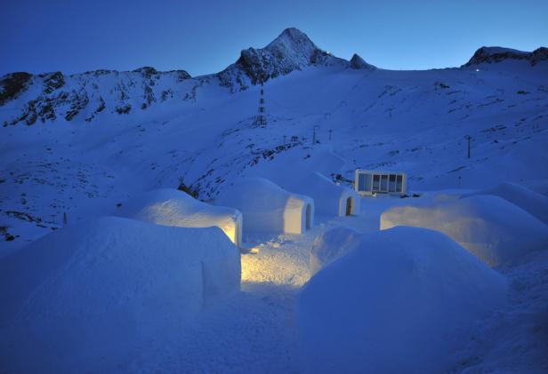 Iglus stehen im Schnee vor einer Bergkulisse.