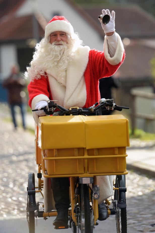 Ein Weihnachtsmann fährt mit einem gelben Lastenfahrrad und klingelt mit einer Glocke.