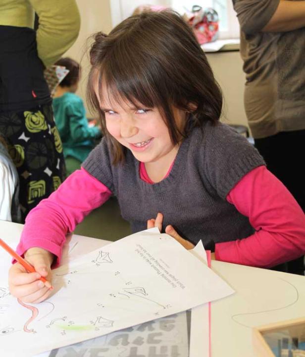 Ein Mädchen mit dunklen Haaren malt mit einem Farbstift auf einem Blatt Papier.