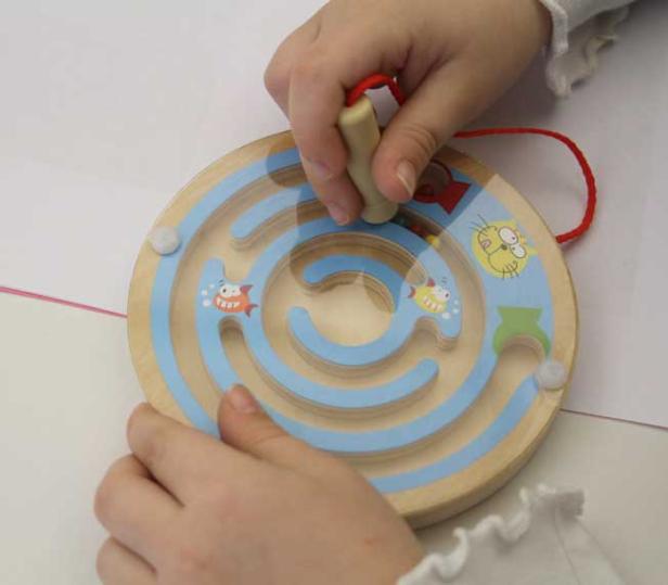 Ein Kind spielt mit einem hölzernen Labyrinth-Spielzeug.