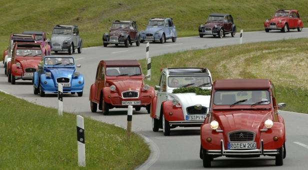 Eine Kolonne von Citroën 2CV Oldtimern fährt auf einer kurvenreichen Straße.