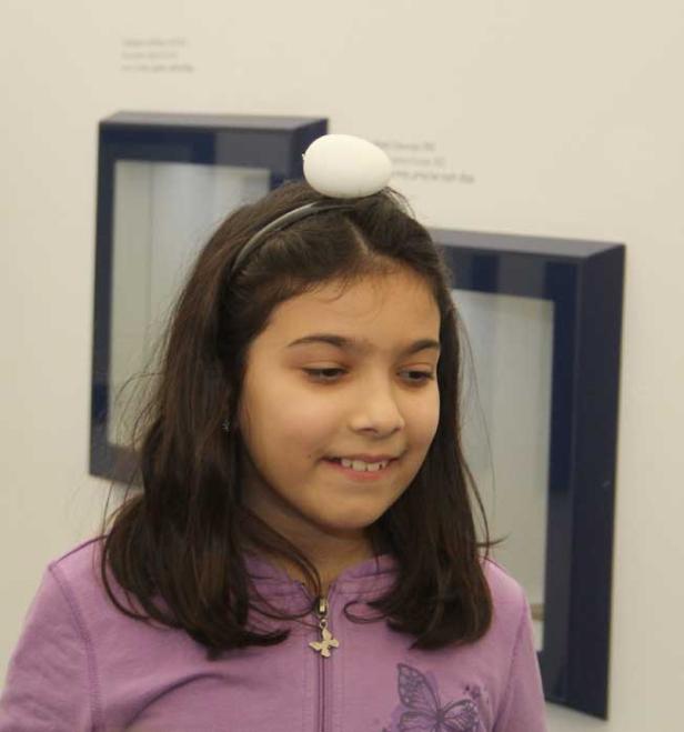 Ein junges Mädchen balanciert ein Ei auf dem Kopf.