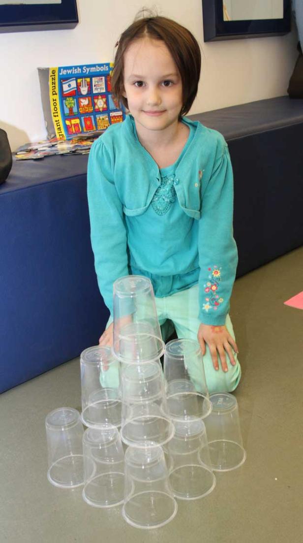 Ein Mädchen kniet vor einem Turm aus Plastikbechern.