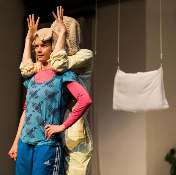 Eine Frau in Sportkleidung steht mit erhobenen Händen vor einer anderen Person mit einem Sack über dem Kopf.