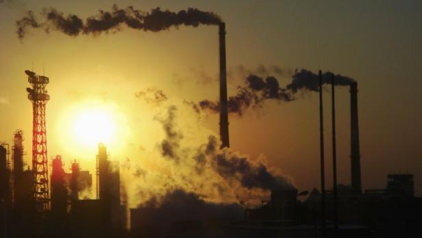 Im goldenen Licht der Abenddämmerung rauchen die Schornsteine einer Industrieanlage.