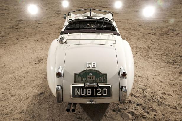 Die Rückansicht eines weißen Oldtimer-Rennwagens mit dem Kennzeichen NUB 120 auf sandigem Untergrund.