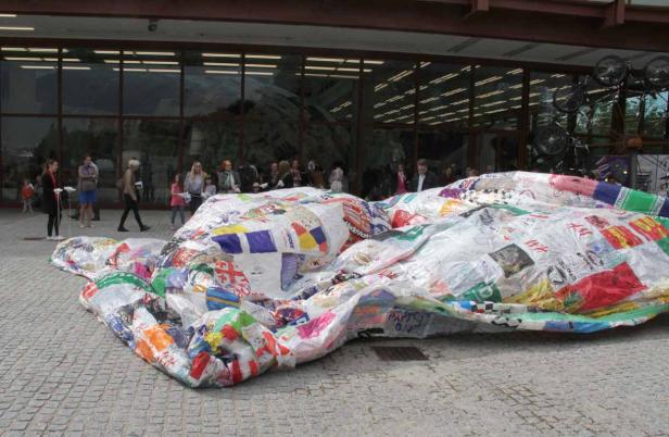 Eine große, aufgeblasene Skulptur aus recycelten Einkaufstüten liegt auf einem Platz.