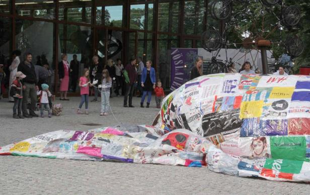 Eine Installation aus recycelten Materialien vor einem Gebäude mit Menschen im Hintergrund.