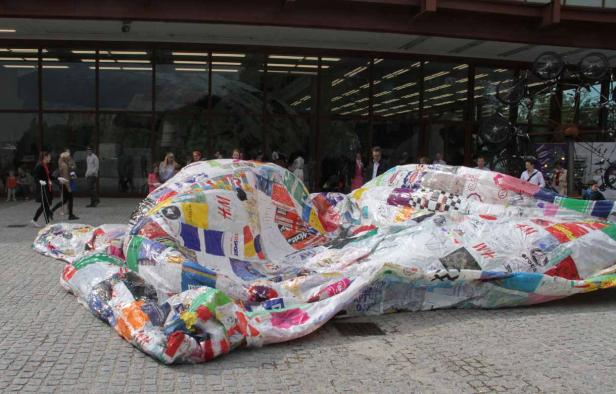 Eine große, aufgeblasene Skulptur aus recycelten Einkaufstüten liegt auf einem Platz.