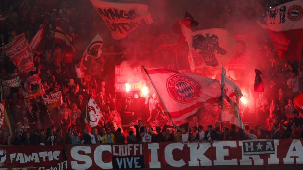 Eine Menschenmenge mit Fahnen und roter Pyrotechnik bei einem Fußballspiel des FC Bayern München.