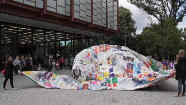 Eine große Schnecken-Skulptur aus recycelten Materialien steht vor einem Gebäude.