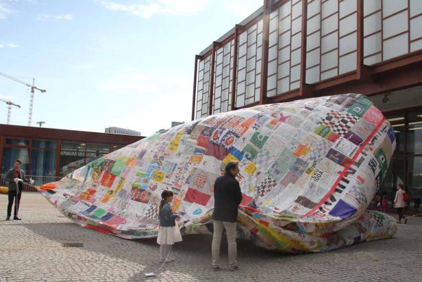 Eine Gruppe von Menschen steht vor einer großen, patchworkartigen Installation im Freien.