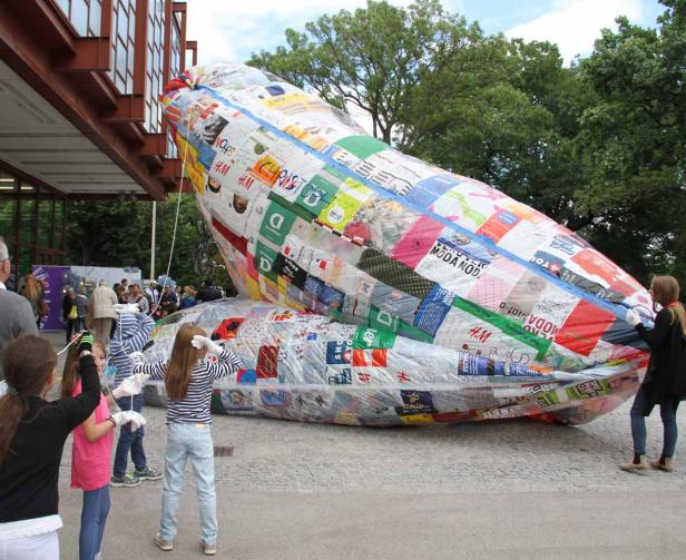Kinder betrachten ein großes, mit Werbeaufdrucken versehenes Luftschiff.