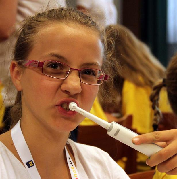 Ein junges Mädchen putzt sich mit einer elektrischen Zahnbürste die Zähne.