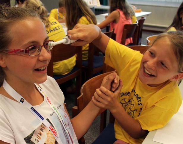 Ein Mädchen hält einem anderen Mädchen eine elektrische Zahnbürste an die Brille.
