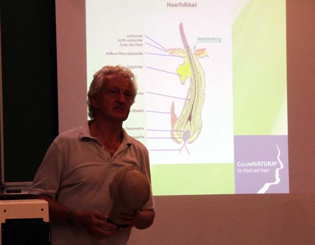 Ein Mann präsentiert eine Grafik des Haarfollikels und ein Modell eines Kopfes.