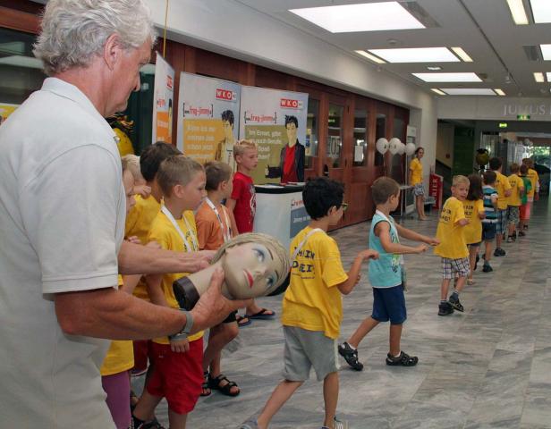 Eine Gruppe Kinder steht Schlange, während ein Mann eine Schaufensterpuppe hält.
