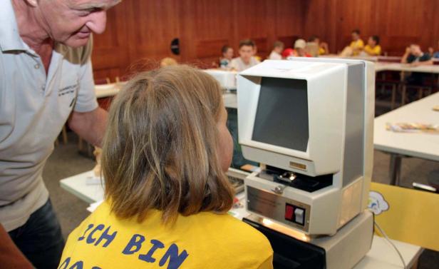 Ein Mädchen bedient ein Gerät, während ein Mann ihr über die Schulter schaut.