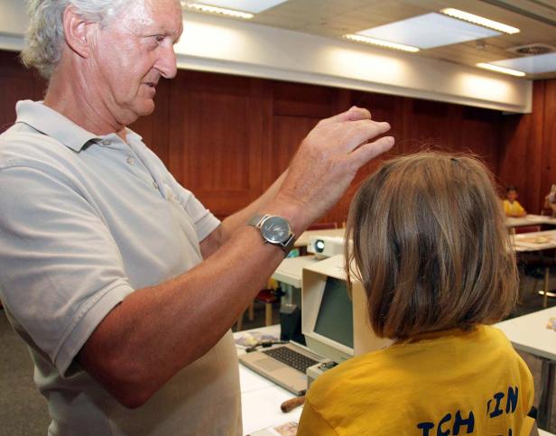 Ein Mann untersucht den Kopf eines Kindes in einem Klassenzimmer.