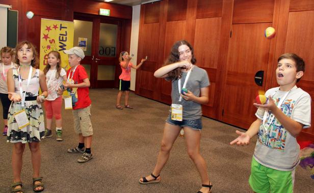 Eine Gruppe Kinder übt sich im Jonglieren mit bunten Bällen in einem Raum.