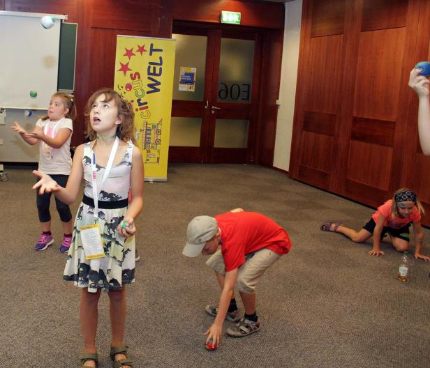Eine Gruppe Kinder übt sich im Jonglieren mit Bällen in einem Raum.