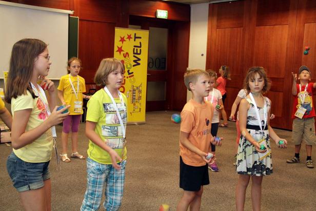 Eine Gruppe Kinder übt sich im Jonglieren mit Bällen in einem Raum.