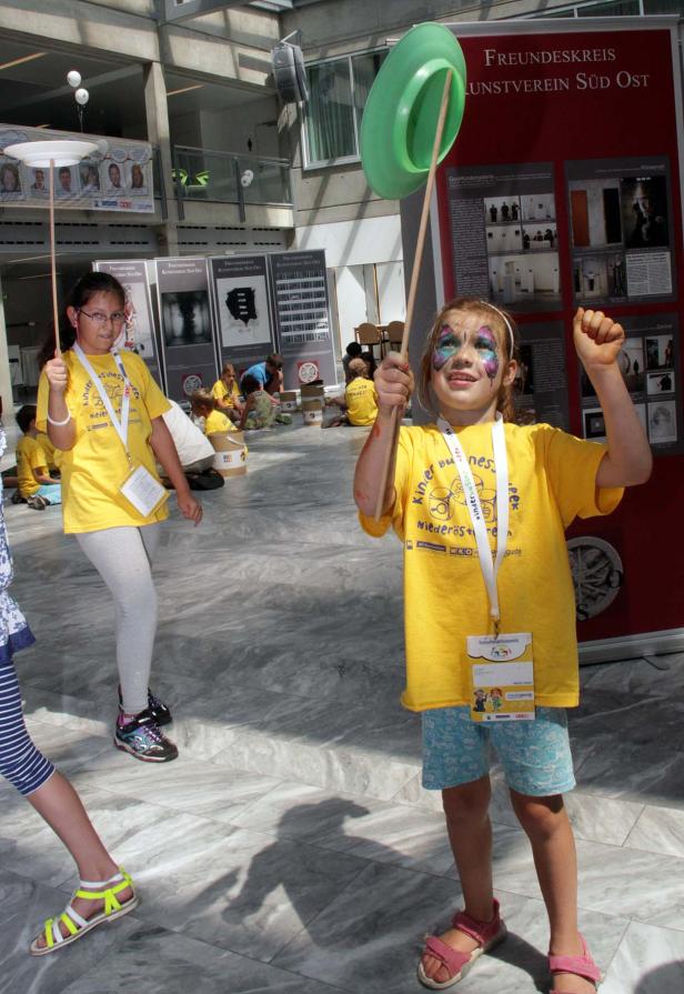 Zwei Mädchen balancieren Teller auf Stäben in einem hellen Raum.