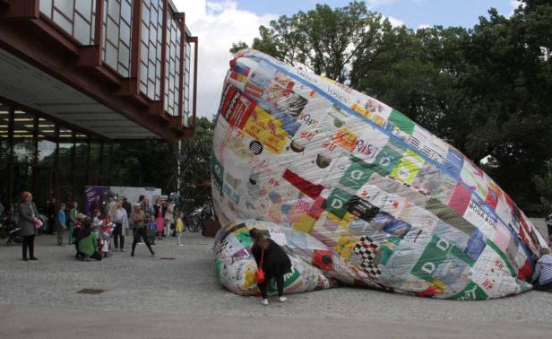Eine große, mit Logos beklebte Installation im Freien zieht die Aufmerksamkeit einer Gruppe von Menschen auf sich.