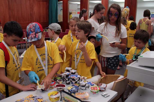 Eine Gruppe Kinder in gelben T-Shirts isst und bastelt an einem Tisch.