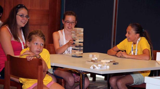 Vier Mädchen sitzen an einem Tisch und spielen ein Geschicklichkeitsspiel mit Holzklötzen.