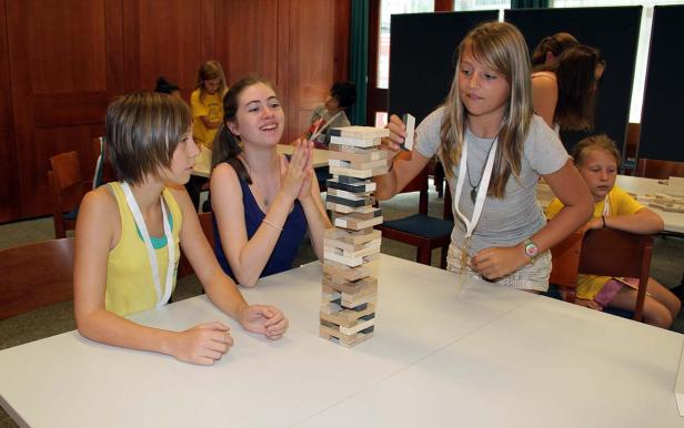 Mehrere Mädchen spielen ein Geschicklichkeitsspiel mit Holzklötzen an einem Tisch.