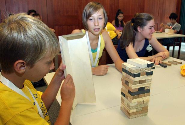 Kinder spielen mit Holzbausteinen und einem Holzrahmen an einem Tisch.